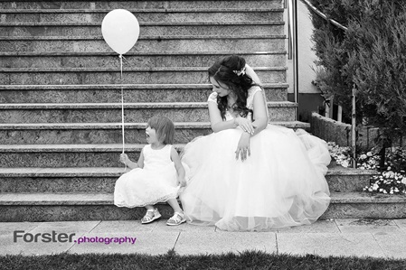 Eine Braut im Kleid sitzt beim Fotoshooting mit einem kleinen Kind auf der Treppe, das Kind hat einen Luftballon