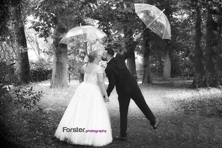 Hochzeitspaar beim Fotoshooting im Wald mit Regenschirmen, der Bräutigam springt und küsst seine Braut