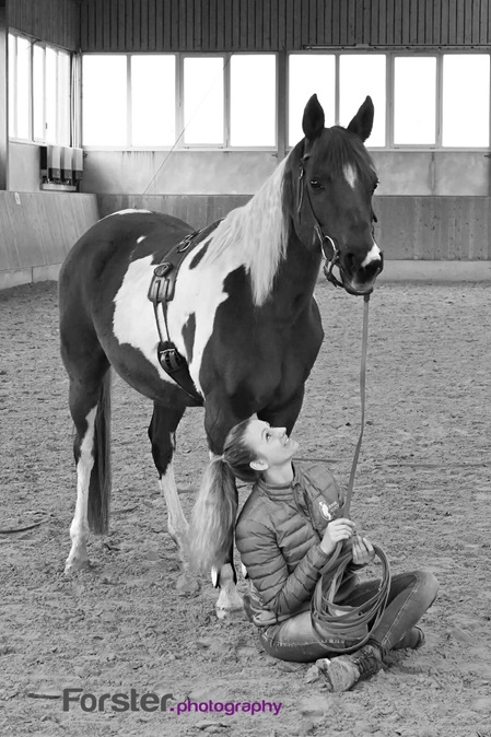 Junge Frau sitzt unter einem Pferd in einem Longierzirkel bei einem Fotoshooting in Iserlohn.