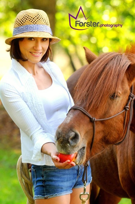 Junge Frau mit Stohhut gibt einem braunen Pferd einen roten Apfel.