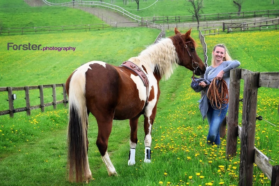 Junge blonde Frau steht mit einem braunen Pferd auf einer grünen Koppel bei einem Fotoshooting in Iserlohn.