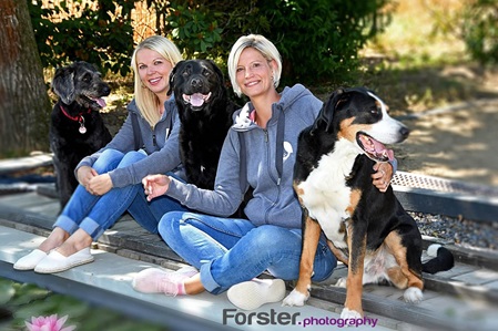 Zwei junge Frauen sitzen mit 2 großen Hunden am Pool.