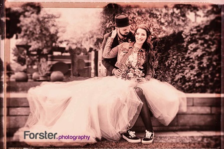 Ein Brautpaar im Hochzeits-Outfit sitzt beim Fotoshooting nebeneinander in einem Park und lächelt in die Kamera