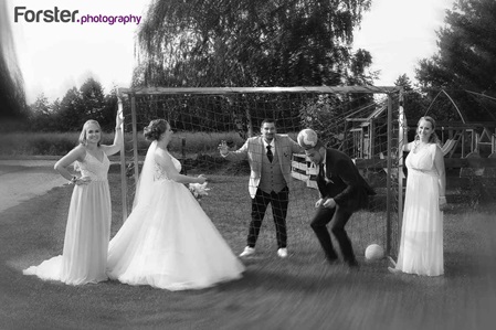Ein Brautpaar im Hochzeits-Outfit spielt beim Fotoshooting mit den Trauzeugen zusammen Fußball