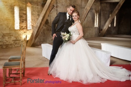 Ein Brautpaar im Hochzeits-Outfit beim Fotoshooting steht in einer Scheune und schaut glücklich in die Kamera