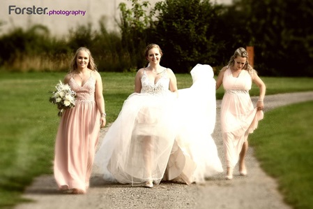 Eine Braut im weißen Hochzeitskleid läuft mit ihren Brautjungfern im Park beim Fotoshooting der Kamera entgegen