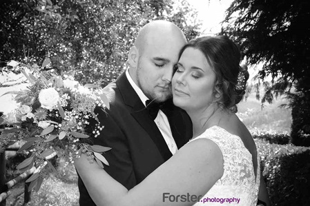 Ein Brautpaar im Hochzeits-Outfit steht beim Fotoshooting dicht zusammen und schließt die Augen