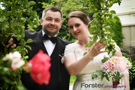 Ein Brautpaar im Hochzeits-Outfit steht beim Fotoshooting dicht zusammen und schauen in die Kamera