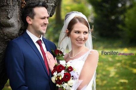 Ein Brautpaar im Hochzeits-Outfit steht beim Fotoshooting dicht zusammen und lächeln