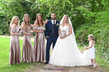Ein Brautpaar im Hochzeits-Outfit posiert beim Fotoshooting in einem Park mit den Brautjungfern
