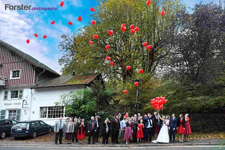 Eine Hochzeitsgesellschaft steht während der Feier vor dem Lokal und lassen rote Luftballons aufsteigen