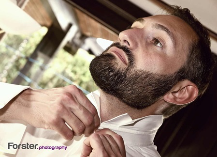 Bräutigam steht vor der Hochzeit beim getting ready Fotoshooting im Wohnzimmer und knöpft sein Hemd zu