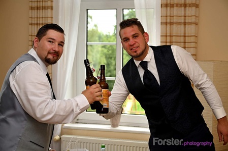 Bräutigam steht vor der Hochzeit beim getting ready Fotoshooting im Wohnzimmer und trinkt Bier mit dem Trauzeugen