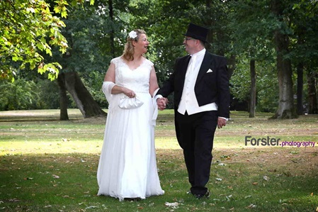 Elegantes Brautpaar geht lächelnd beim Hochzeits-Fotoshooting Hand in Hand, der Bräutigam trägt einen Zylinder