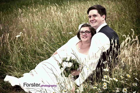 Ein Brautpaar liegt beim Hochzeits-Fotoshooting nebeneinander im Gras und lächelt in die Kamera