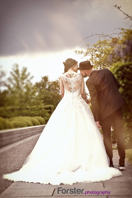 Ein Brautpaar steht beim Hochzeits-Fotoshooting dicht zusammen, er küsst ihre Schulter