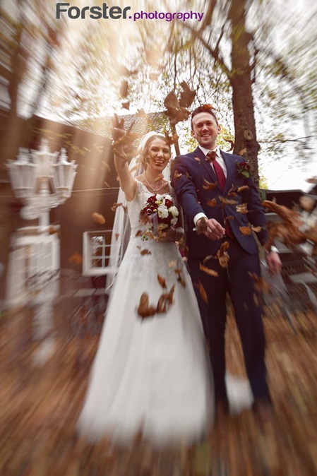 Ein Brautpaar steht beim Hochzeits-Fotoshooting nebeneinander in einem Garten und werfen Laub in die Höhe