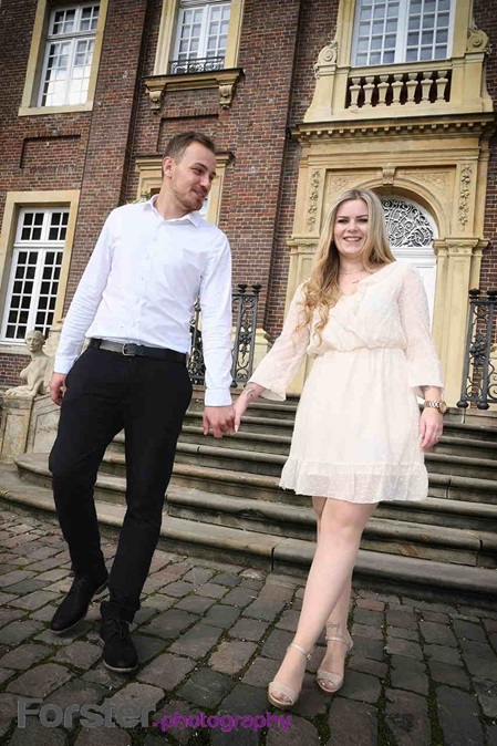 Ein Brautpaar im Hochzeits-Outfit geht beim Fotoshooting Hand in Hand eine Treppe hinab und lächelt in die Kamera