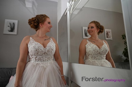 Eine Braut steht vor der Hochzeit beim getting ready Fotoshooting vor dem Spiegel und lächelt