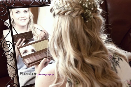 Eine Braut sitzt vor der Hochzeit beim getting ready Fotoshooting vor einem Spiegel und schminkt sich