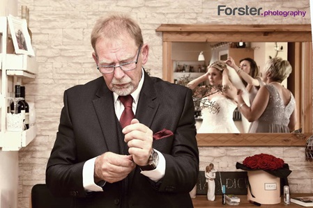 Eine Braut beim getting ready Fotoshooting, im Vordergrund steht der Brautvater beim Ankleiden