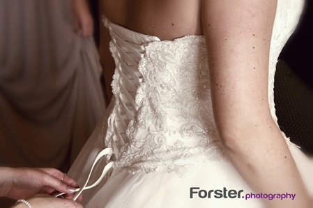 Einer Braut wird vor der Hochzeit beim getting ready Fotoshooting das Brautkleid mit Hilfe der Trauzeugin angezogen