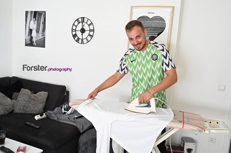 Ein Bräutigam steht vor der Hochzeit beim getting ready Fotoshooting im Wohnzimmer und bügelt sein Oberhemd