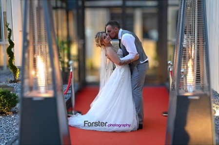 Hochzeitspaar küsst sich verliebt beim Fotoshooting auf einem roten Teppich vor zwei Flammen