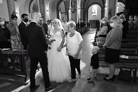 Hochzeitspaar in der Kirche, die Braut wird von der Mutter zum Altar geführt. Der Ehemann wartet gespannt