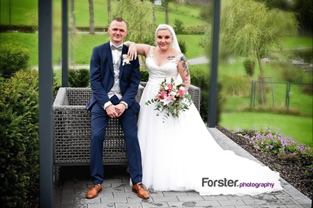 Hochzeitspaar sitzt beim Fotoshooting nebeneinander, die Braut legt ihren Arm auf die Schulter des Bräutigams