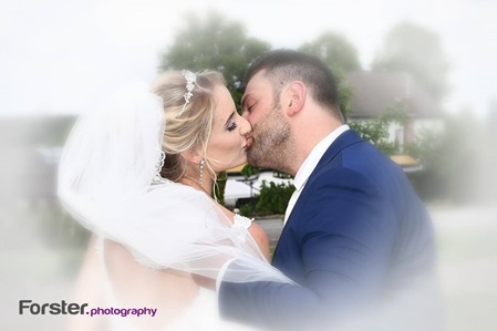 Eine Braut im weißen Hochzeitskleid mit langem Schleier küsst ihren Bräutigam beim Fotoshooting innig