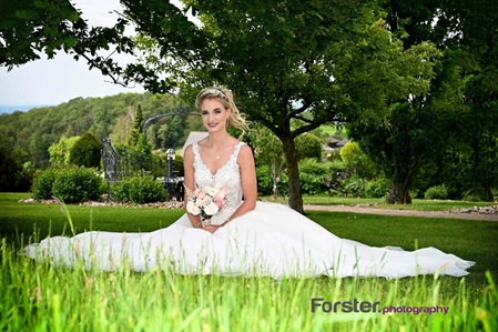 Eine Braut sitzt beim Fotoshooting alleine mit Brautstrauß auf einer Wiese. Das weiße Kleid ist ausgebreitet