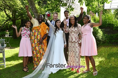 Ein Brautpaar im steht beim Hochzeits-Fotoshooting zusammen mit einer Gästegruppe, alle winken fröhlich in die Kamera