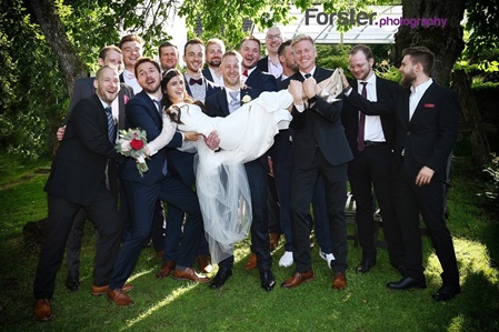 Ein Braut wird beim Fotoshooting vom Bräutigam und seinen Freunden hochgehoben, alle lachen in die Kamera