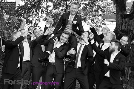 Ein Bräutigam wird beim Fotoshooting von seinen Freunden auf den Schultern getragen, alle lachen in die Kamera