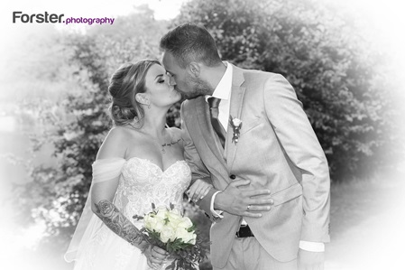 Ein Brautpaar im Hochzeits-Outfit beim Fotoshooting schaut sich verliebt an und küsst sich