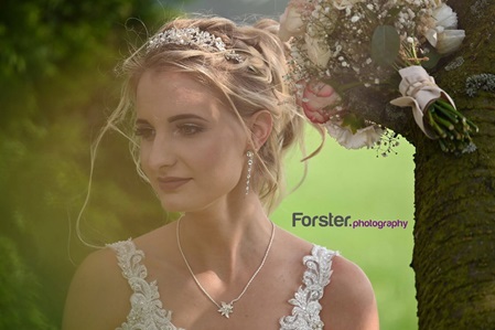 Eine Braut sitzt beim Fotoshooting im weißen Hochzeitskleid an einem Baum und schaut zur Seite