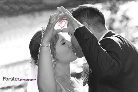 Eine Braut im weißen Hochzeitskleid beim Fotoshooting an einem Fluss. Sie formen zusammen mit ihren Händen ein Herz