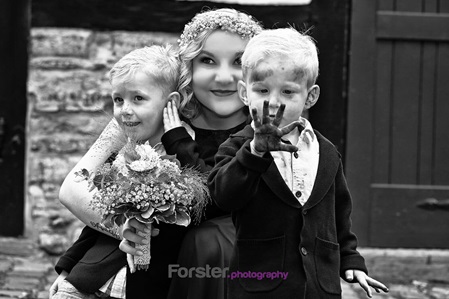 Eine Braut sitzt beim Fotoshooting mit zwei Kindern auf dem Boden. Die Kinder haben sehr dreckige Hände