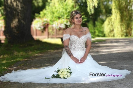 Eine Braut sitzt beim Fotoshooting alleine mit Brautstrauß in einem Park. Das weiße Kleid ist ausgebreitet