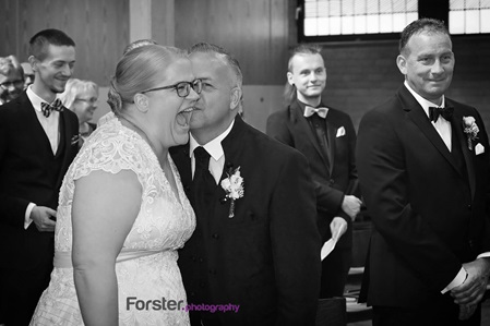 Ein Hochzeitspaar bei der Trauung in der Kirche. Der Bräutigam flüstert der laut lachenden Braut etwas ins Ohr