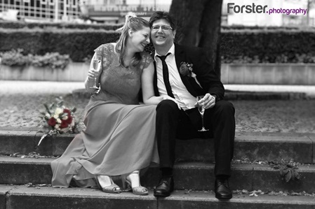 Ein Brautpaar im Hochzeits-Outfit beim Fotoshooting sitzt auf einer Treppe und lächelt verliebt