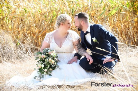 Ein Hochzeitspaar sitzt beim Fotoshooting in einem Kornfeld und blickt sich verliebt in die Augen