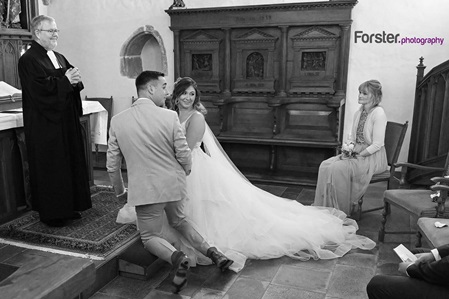 Ein Brautpaar kniet an der Hochzeit am Altar vor dem Pastor und blickt gemeinsam nach hinten