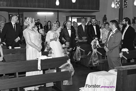 Eine Braut wird vom Vater in der Kirche an der Hochzeit zum Altar geführt. Der Bräutigam wartet vorne gespannt