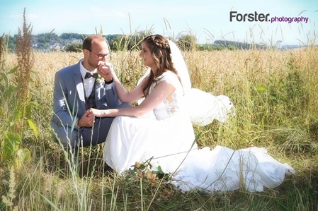 Brautpaar sitzt am Hochzeitstag in einem Kornfeld beim Fotoshooting. Der Ehemann küsst verliebt die Hand der Braut.