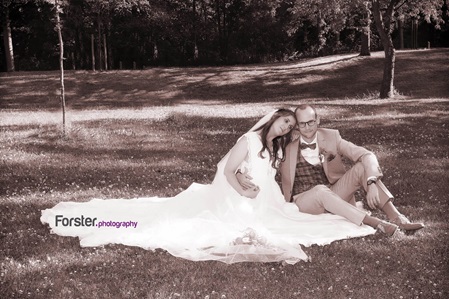 Ein Brautpaar sitzt beim Fotoshooting auf einer Wiese nebeneinander. Das weiße Brautkleid ist ausgebreitet