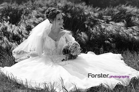 Braut beim Fotoshooting sitzt an ihrem Hochzeitstag alleine in einem Kornfeld mit ihrem Brautstrauß