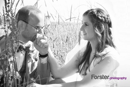 Brautpaar sitzt am Hochzeitstag in einem Kornfeld beim Fotoshooting. Der Ehemann küsst verliebt die Hand der Braut.