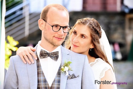 Brautpaar im Outfit am Hochzeitstag beim Fotoshooting. Die Braut schaut ihrem Ehemann verliebt über die Schulter.